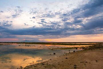 View of low tide of the Indian ocean and the outline of the island Bali and mount and volcano Gunung Agung from the beach of Gili Trawangan, Indonesia. Seascape at sunset. Reflection in water. 