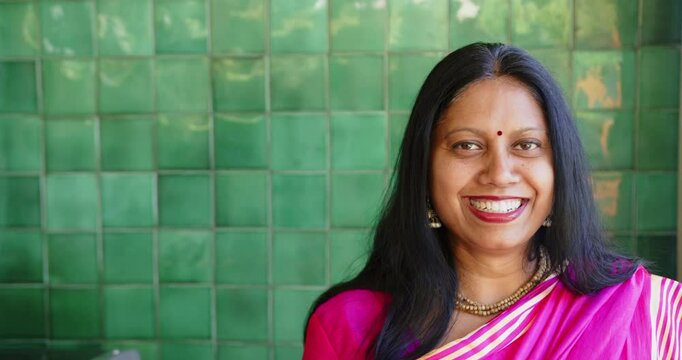 Smiling Indian woman in traditional Indian sari standing against green tiled wall, copy space