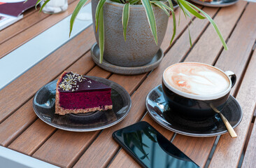 cup of cappuccino , delicious berry cake, and smartphone placed on table at an outdoor café, cozy and relaxing moment in a charming urban setting, enjoying coffee and dessert while staying connected