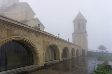 Tiled church courtyard, lower part with rooms, bell tower in the fog
