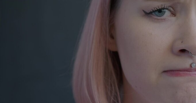 Close-up portrait of miserable young woman half face feeling sad looking at camera on black background. People and negative emotion concept.