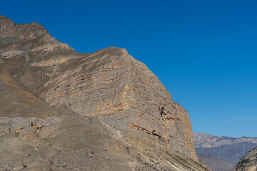 Fototapeta premium Kabardino-Balkaria. El-Tyubu. Rocky mountains with trees growing on their slopes glow in morning sun. Close-up. Chegem Gorge. Unique rocky ridge with steep cliffs against blue autumn sky.