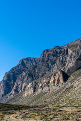 Fototapeta premium Kabardino-Balkaria. El-Tyubu. Rocky mountains with trees growing on their slopes glow in morning sun. Close-up. Chegem Gorge. Unique rocky ridge with steep cliffs against blue autumn sky.