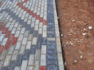 Close-up of a decorative brick sidewalk design under construction, featuring contrasting red and grey blocks