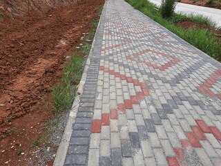 constructed brick walkway featuring red and grey patterns, with soil and small plants visible along the edge