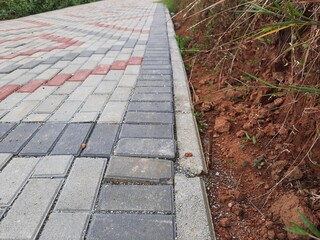 Detailed view of a patterned sidewalk made of interlocking bricks, accompanied by exposed soil and scattered greenery
