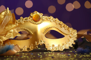 Beautiful carnival mask, ribbons and confetti on color background with blurred lights, closeup