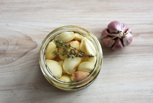 Garlic cloves pickled in sunflower oil and thyme. A glass jar full of garlic cloves should be kept in the refrigerator. Flat lay.