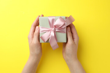 Woman holding gift box with pink bow on yellow background, top view
