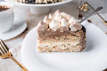 Kyiv cake with nuts, buttercream on a white cake pan in a cut on a white plate, espresso coffee, gold cutlery, Ukrainian desserts, nut cake, flatlay