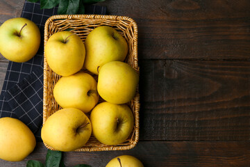 Fresh yellow apples in wicker basket on wooden table, top view. Space for text