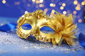 Beautiful carnival mask on blue glitter background against blurred lights, closeup. Bokeh effect