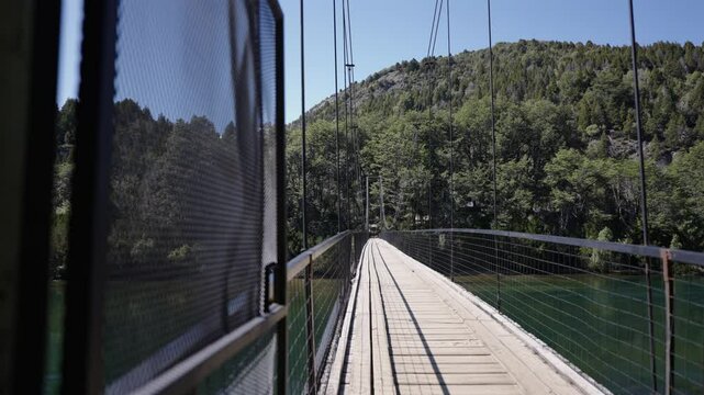 A suspension bridge crosses a turquoise river, surrounded by lush green forest