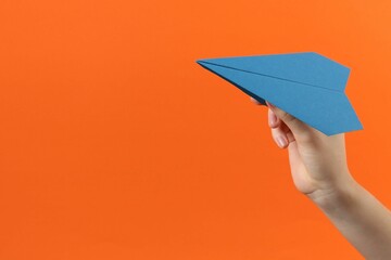 Woman with blue paper plane on orange background, closeup. Space for text