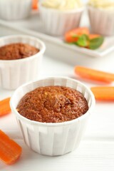 Delicious carrot muffins and fresh vegetables on white wooden table, closeup