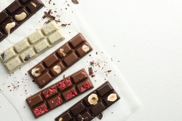 Tasty chocolate bars and crumbs on white textured background, flat lay. Space for text
