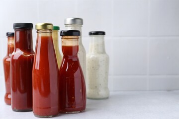 Tasty sauces in glass bottles on white table, closeup. Space for text