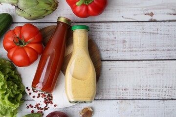 Tasty sauces in glass bottles and fresh products on white wooden table, flat lay. Space for text