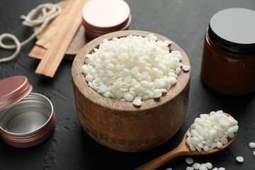 Soy wax in bowl, candle, wooden wicks, twine and jars on black table, closeup