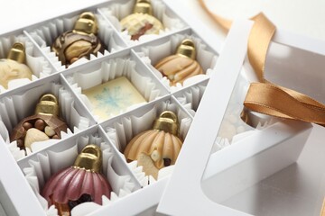 Box with tasty chocolate candies in shape of baubles on white background, closeup