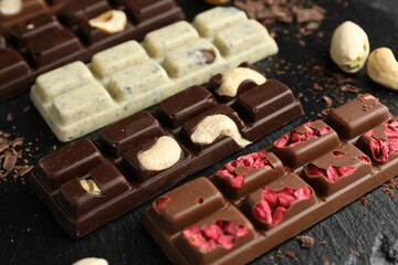 Different tasty chocolate bars with nuts and freeze dried raspberry on black table, closeup