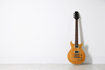 Fototapeta premium One modern electric guitar near white wall. Space for text