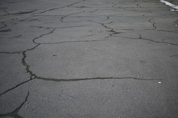 cracks in the asphalt after frost, cracked texture of grey bitumen, road surface covered with snow after winter 