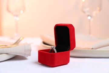 Beautiful engagement ring and setting for romantic dinner on white table, closeup