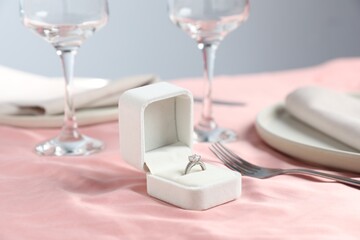 Engagement ring in box and tableware on pink tablecloth, closeup. Romantic dinner