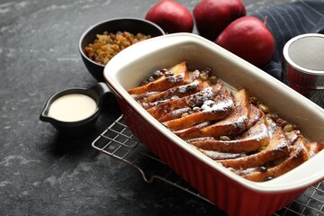 Freshly baked bread pudding in baking dish and products on dark textured table, closeup