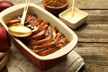 Freshly baked bread pudding in baking dish and spoon on wooden table, closeup