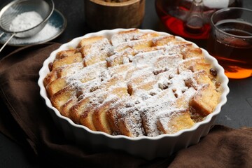 Delicious bread pudding with raisins, powdered sugar and tea on black table, closeup