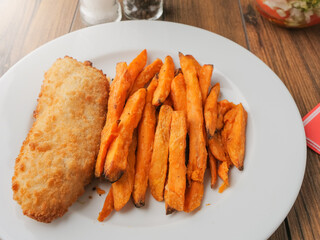 Popular fish and chips meal on a white plate and brown wooden table. Chips are made from sweet...