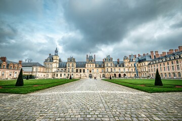 Obraz premium Stunning view of the historic Chateau de Fontainebleau in France under a dramatic cloudy sky