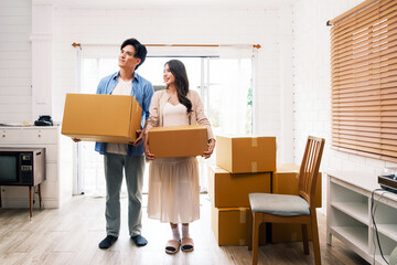 A couple carries moving boxes in a bright, modern living room, symbolizing new beginnings and relocation. An attractive romantic man and woman carry boxes parcel with happiness and love.