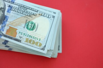 Big amount of hundred dollar bills in thick stack lies on bright red color paper background