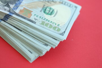 Big amount of hundred dollar bills in thick stack lies on bright red color paper background