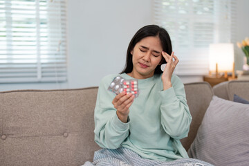 Woman in a mint green sweater sitting at home, feeling unwell while holding a blister pack of...