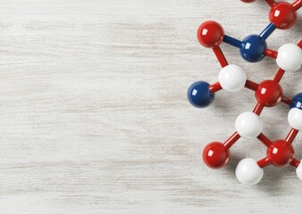 A colorful molecular model with red, white, and blue spheres on a light wooden background, representing atoms and chemical bonding.