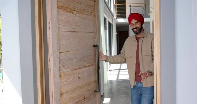 Welcoming guests, man in turban smiling and opening front door of home