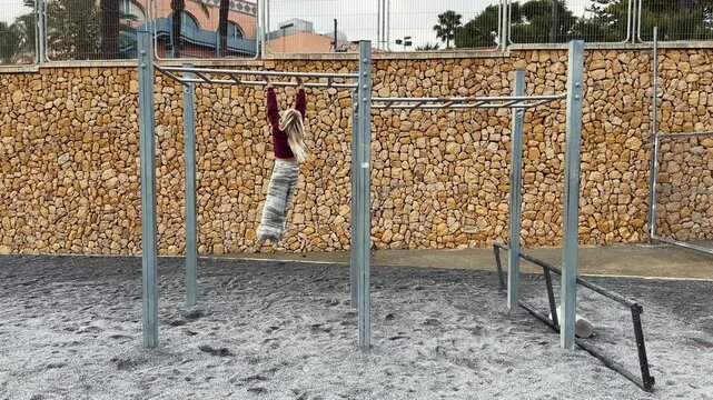 Young girl wearing christmas outfit having fun moving backwards on monkey at a playground. Wide shot