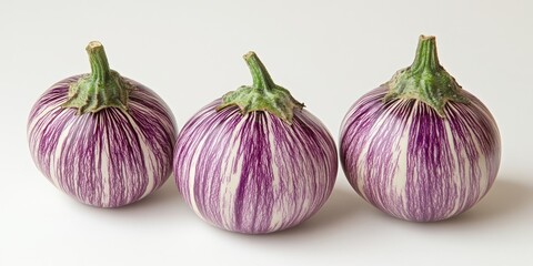 Obraz premium Three small striped eggplants with deep purple and white stripes positioned in a row against a clean white background, showcasing their vibrant colors.