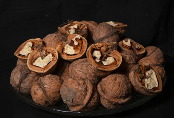 Peeled and whole walnuts lie on a glass plate. Black background.