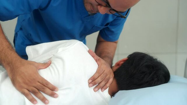 Young physical therapist man massaging patient to relieve and recover back muscle injury for rehabilitation physiotherapy at hospital, young man having chiropractic therapy in hospital room.