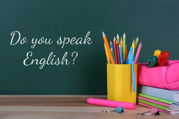 Do You Speak English? text on green chalkboard and stationery on wooden table. Language course
