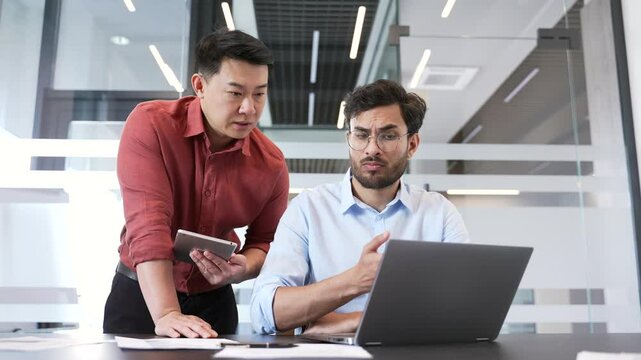 Two colleagues in office discussing project with laptop and tablet. Male manager advises, talking to employee. Business meeting. The boss consults the subordinate worker. Executive explains work issue
