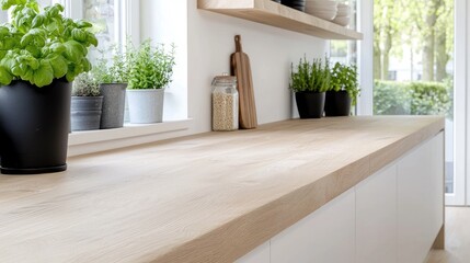 Fototapeta premium Fresh green basil and herbs in pots on a light wooden countertop in a bright modern kitchen.