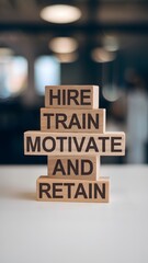 Four wooden blocks stacked on a white surface read "HIRE TRAIN MOTIVATE AND RETAIN" in sans-serif font. A blurred indoor background emphasizes the clear HR message, ideal for business or motivational 