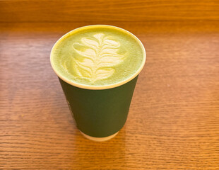 Warm matcha latte with intricate leaf design resting on wooden table in cozy cafe during afternoon