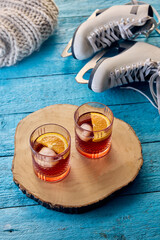 Two glasses of winter beverage with orange slices on wooden tray, ice skates and knitted blanket in background, reflecting festive and creative winter moments. Concept of winter, aesthetic, alcohol.